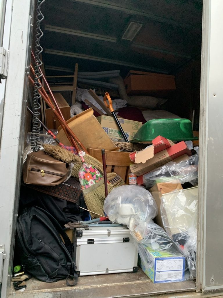 遺品整理のトラックの荷台。杖やほうき、かばん、段ボール箱などが積み上げられている